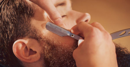 Professional barber shaving beard of his client